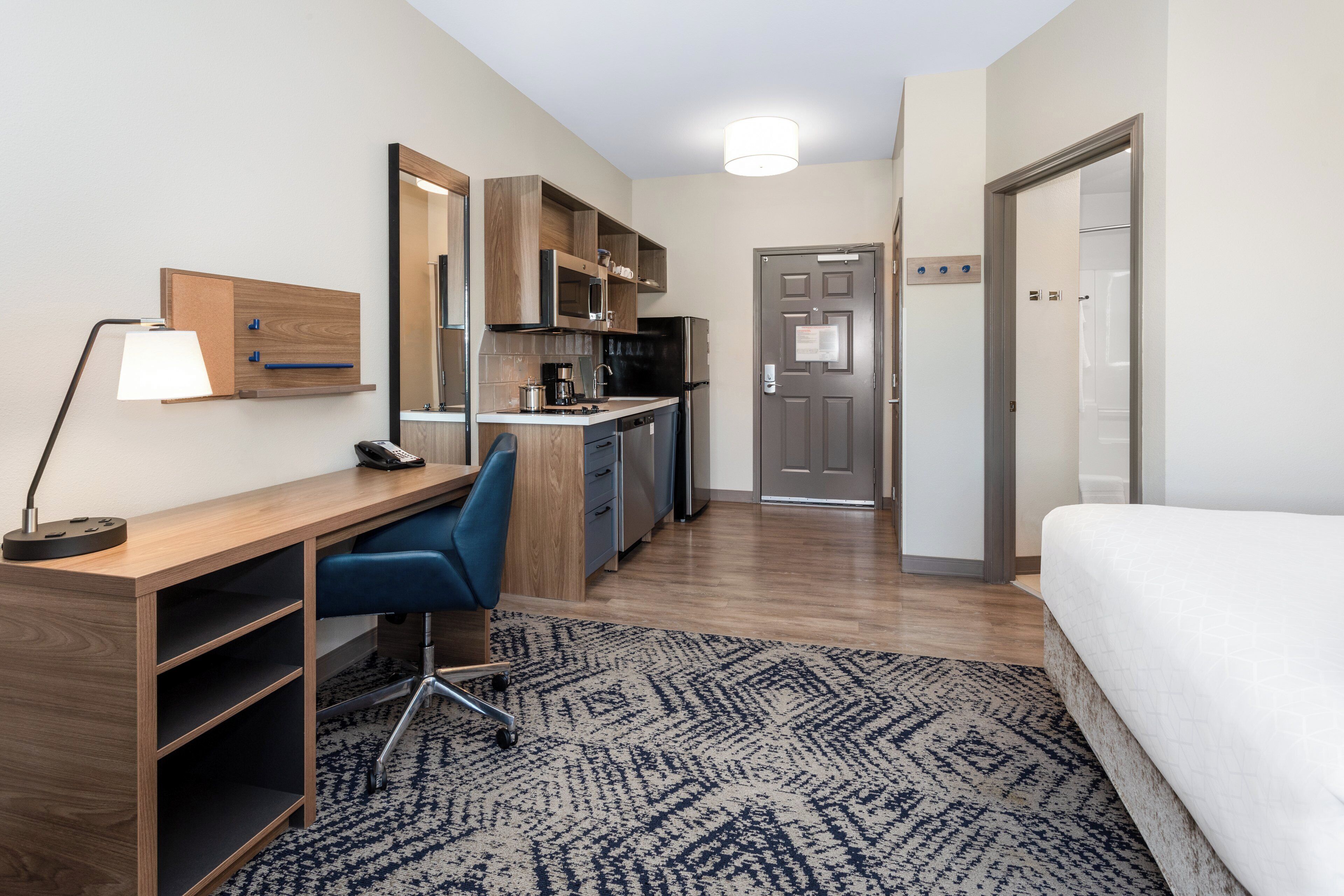 Habitación de hotel compacta con kitchenette, un escritorio con silla, una cama y un tapete estampado.