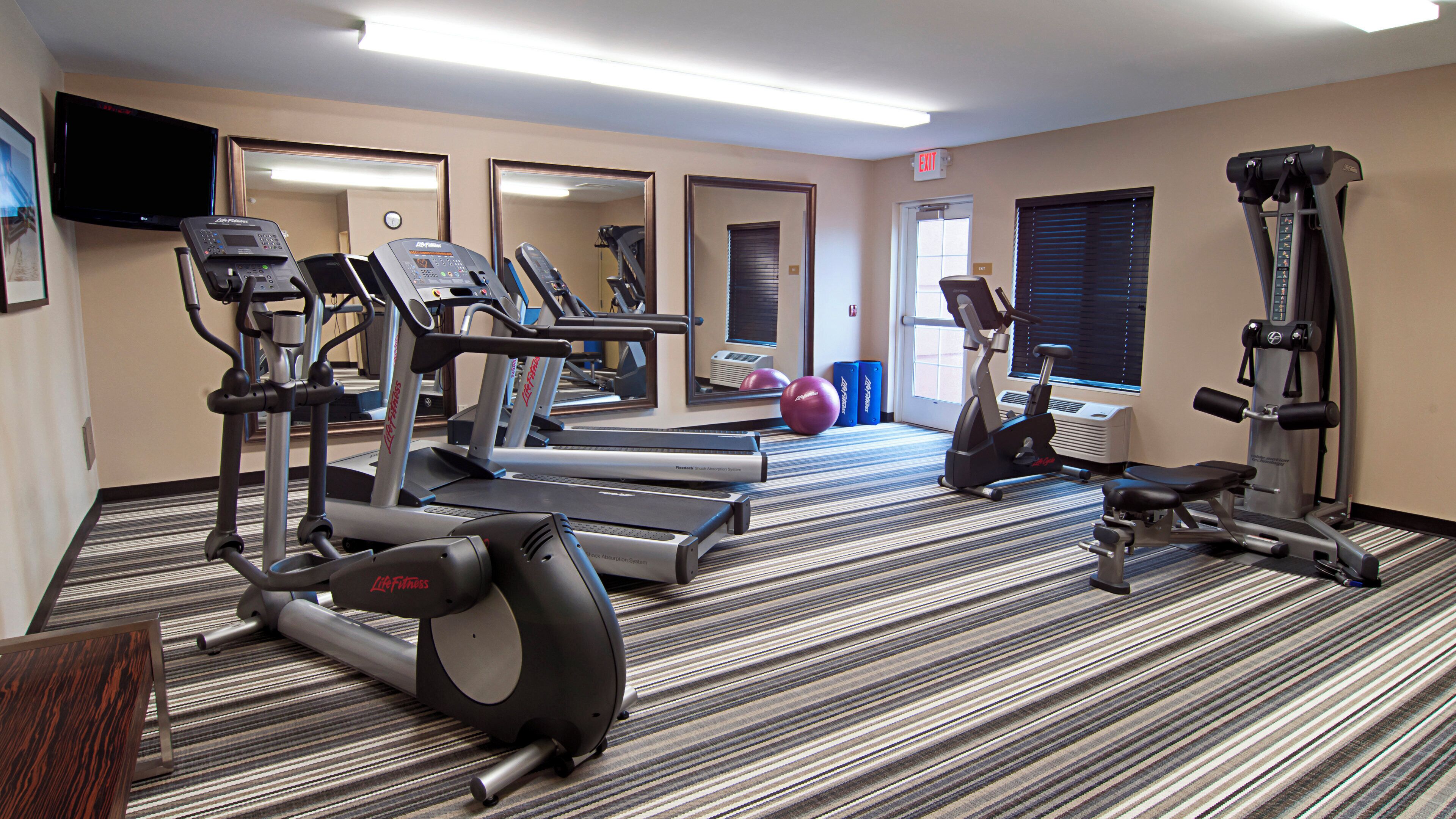 Une salle de sport d’hôtel équipée de machines de cardio, de poids libres et d’un mur avec des miroirs.