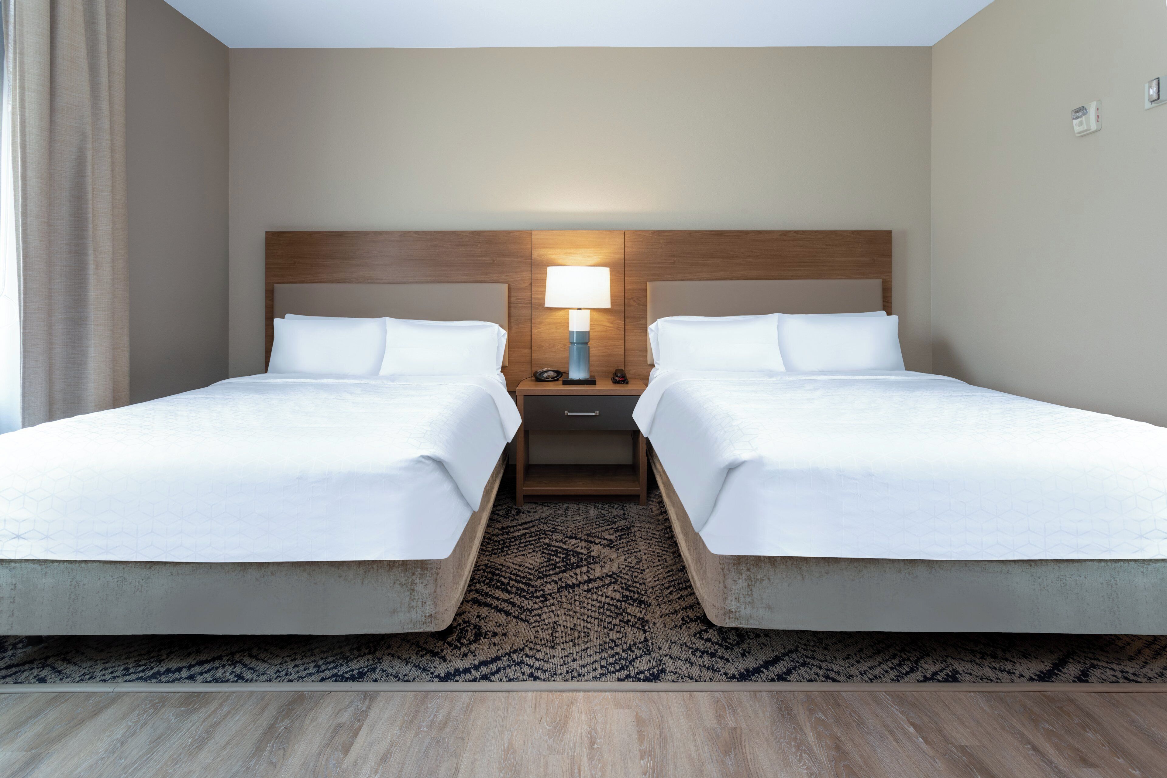 A hotel room with two beds, a nightstand with a lamp, and a patterned rug.