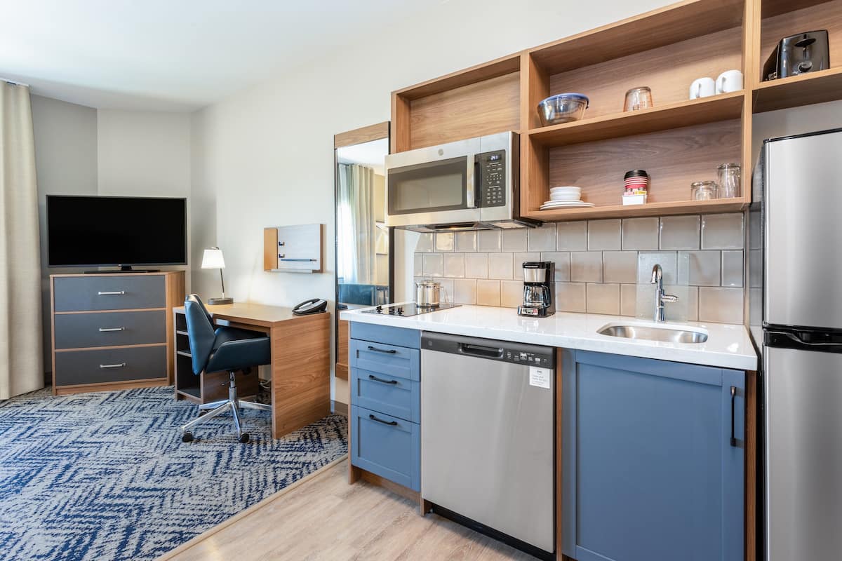 A modern kitchen with a microwave, coffee maker, and dishwasher. There is a TV and a desk with a chair.