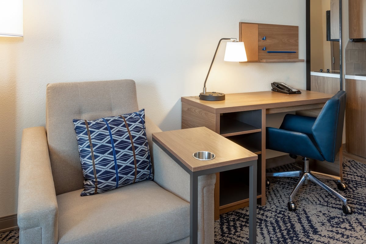 A hotel room with a sofa, a desk with a lamp, a chair, and a small table.