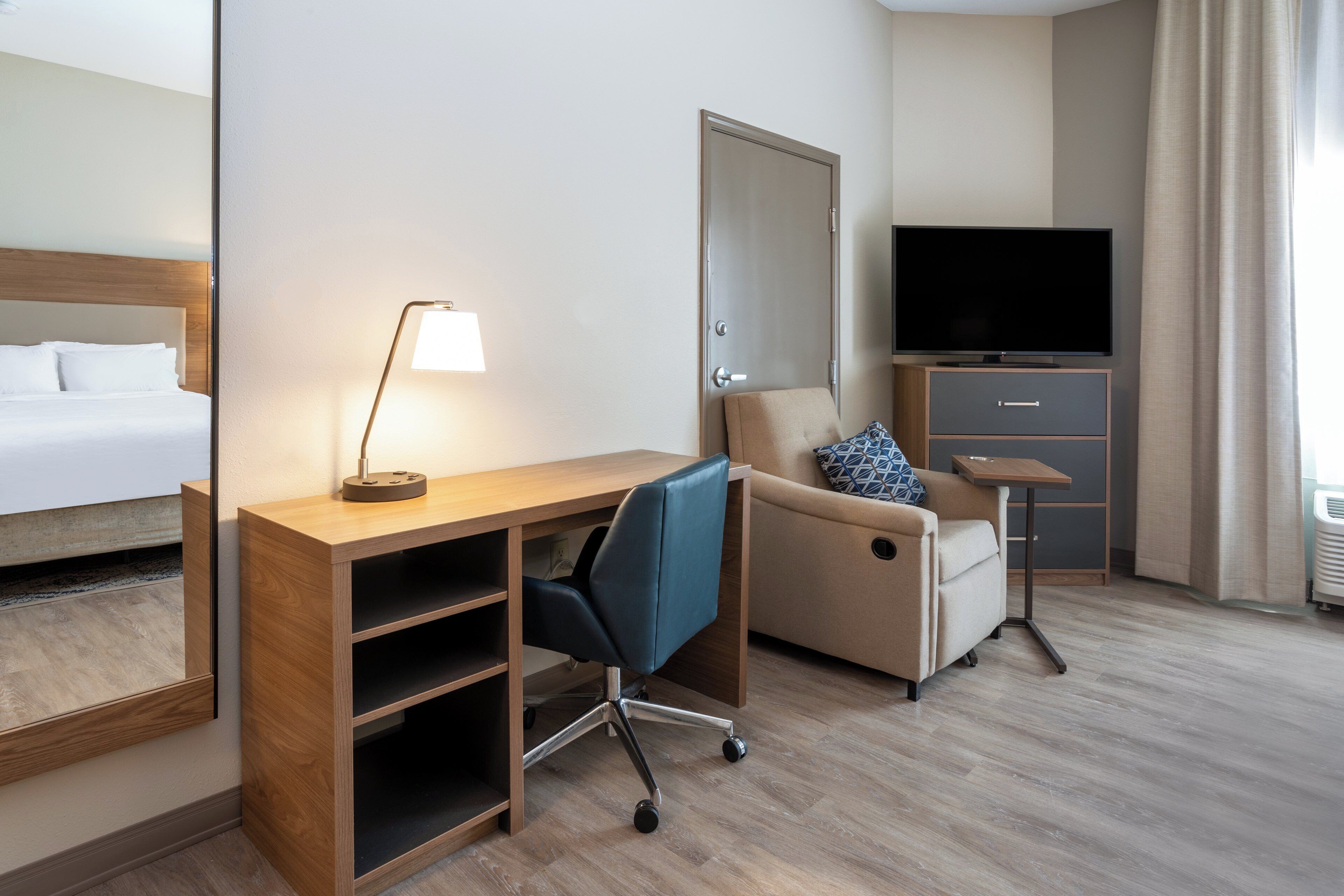 A hotel room with a bed, desk, chair, TV, and a small table.