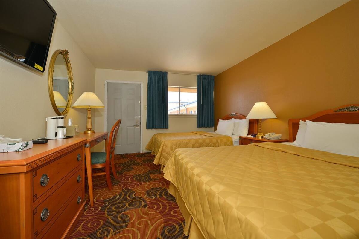 A hotel room with two beds, a desk with a chair, a dresser, a television, and a window with curtains.
