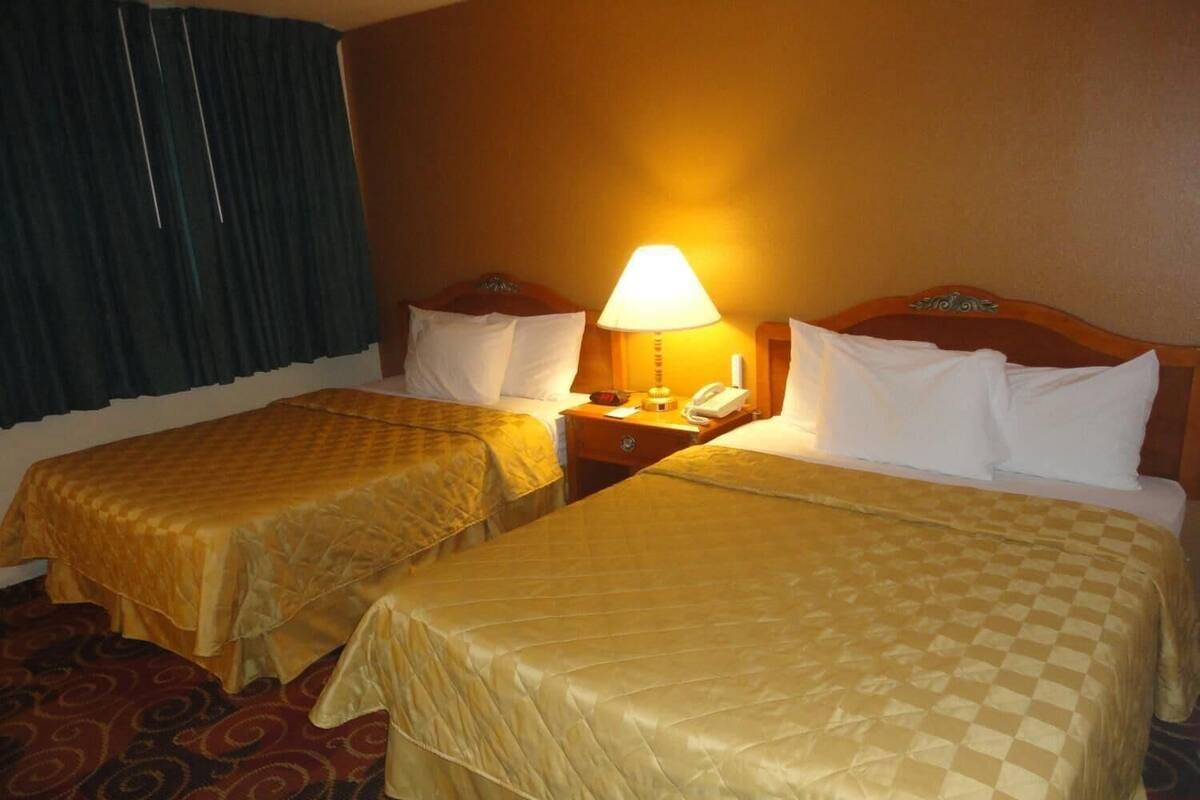 A hotel room with two beds, a nightstand with a lamp, and a telephone.