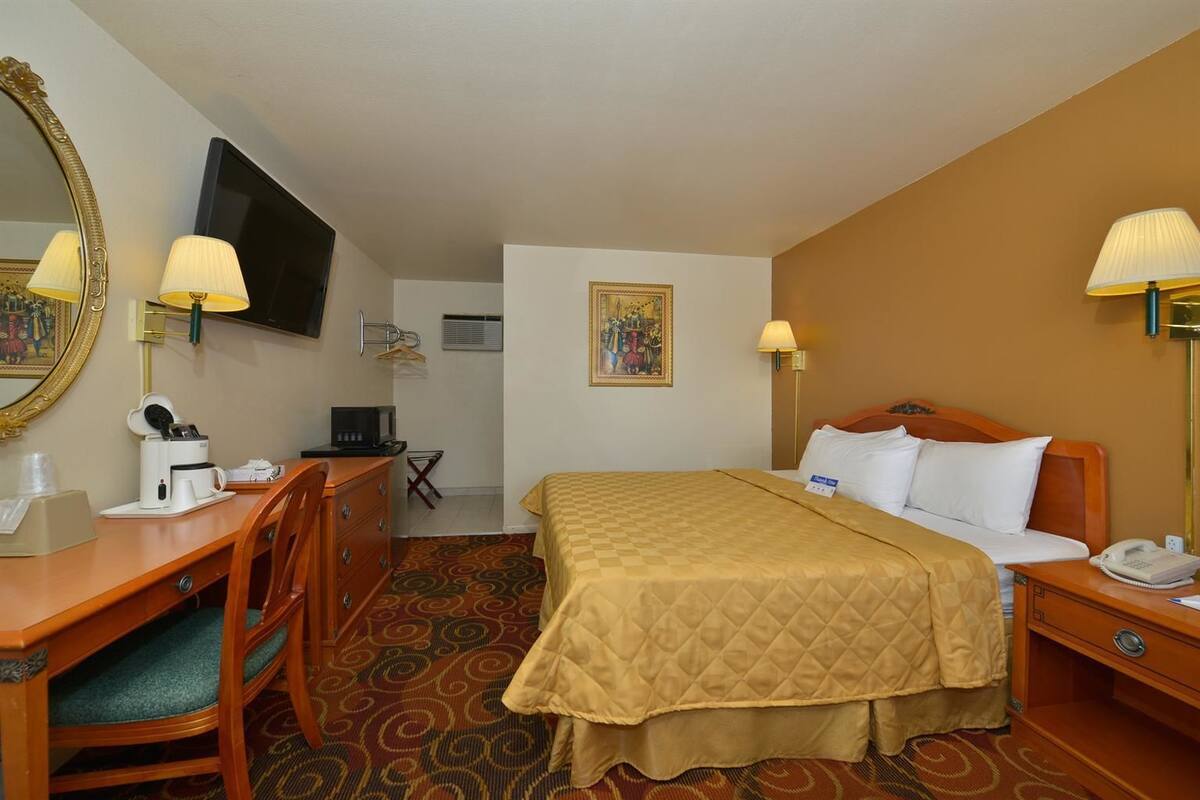 A hotel room with a bed, a desk with a computer, a chair, a mirror, and a television.