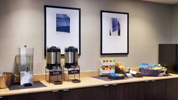 Espaço de café da manhã de hotel, com estação de café, variedade de frutas e um bar de petiscos.