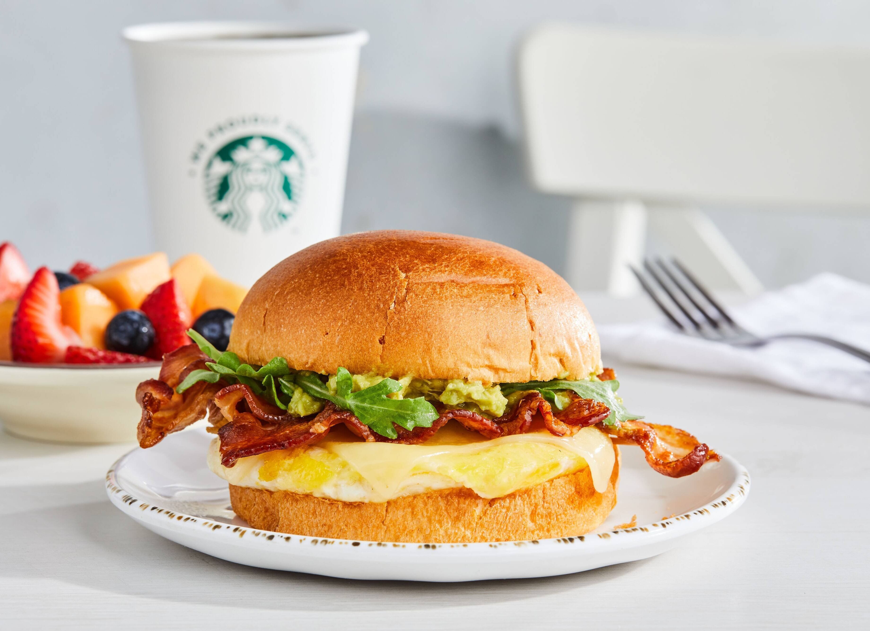 Ein Frühstückssandwich auf einem Teller, im Hintergrund eine Starbucks-Tasse.