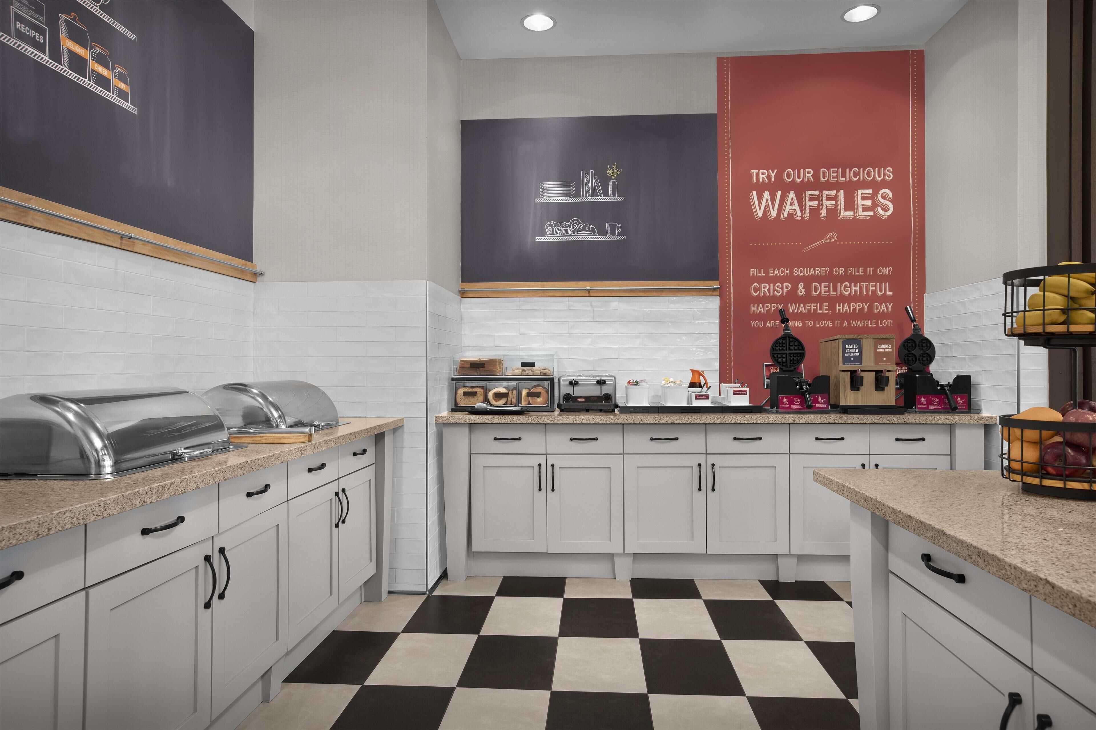 A modern kitchen with white cabinets, a black and white checkered floor, and a large waffle advertisement on the wall.