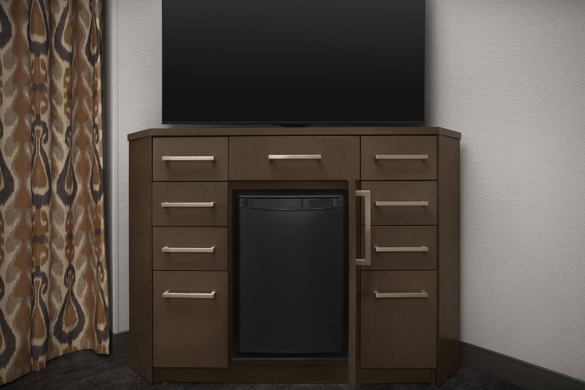 A corner room with a built-in wardrobe, a flat-screen TV mounted above it, and a patterned curtain on the left.