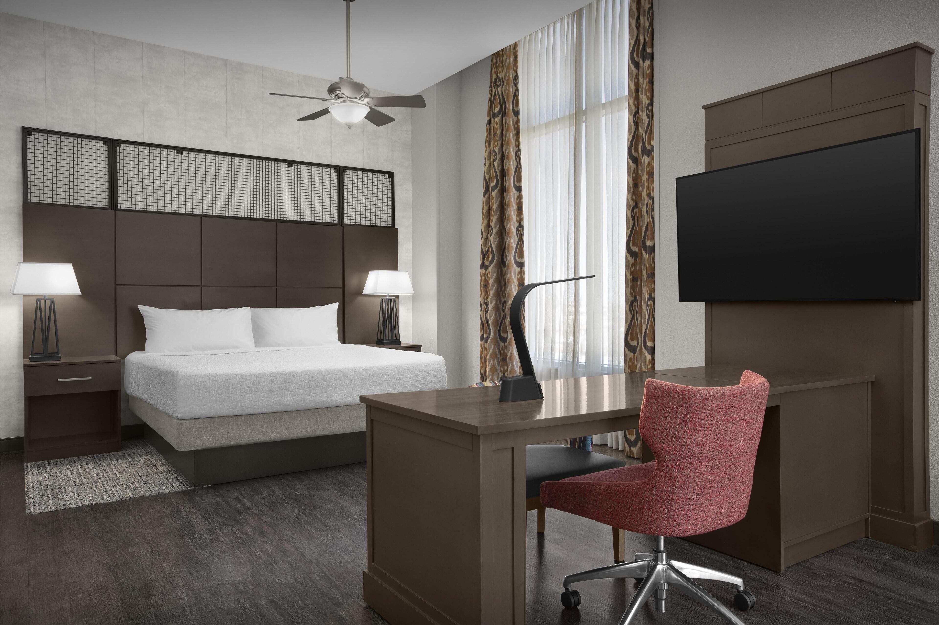 A hotel room with a bed, desk, chair, TV, and a ceiling fan.
