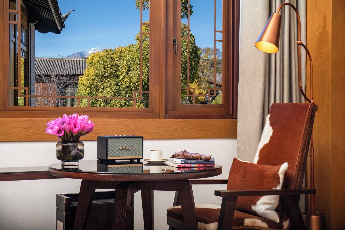A room with a traditional Japanese-style window, a table with a radio and books, a chair, and a vase with flowers.