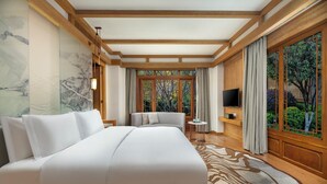 A spacious hotel room with a large bed, a TV, a small table, and a view of greenery through large windows. - Hotel Indigo Lijiang Ancient Town by IHG (Lijiang)