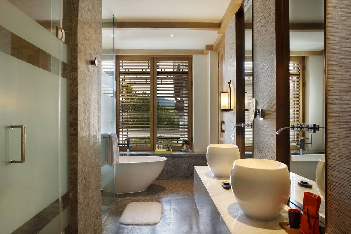 Een moderne badkamer met een vrijstaand bad, twee grote wastafels en een grote spiegel.