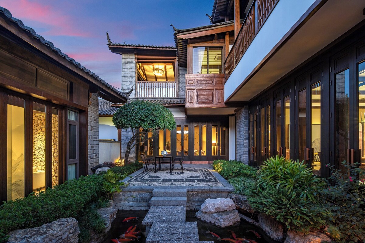 A traditional courtyard with a stone pathway, a small pond, and a wooden table with chairs.