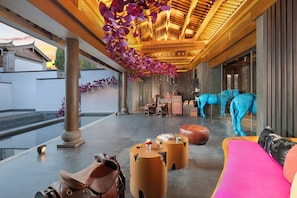 A spacious lobby with a modern design, featuring a large seating area, a reception desk, and decorative elements like a hanging floral arrangement and a unique blue horse sculpture.
