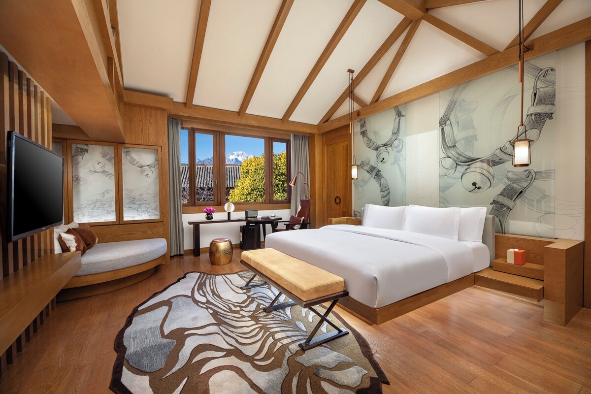 Een moderne hotelkamer met een groot bed, een televisie, een bureau en uitzicht op het groen.