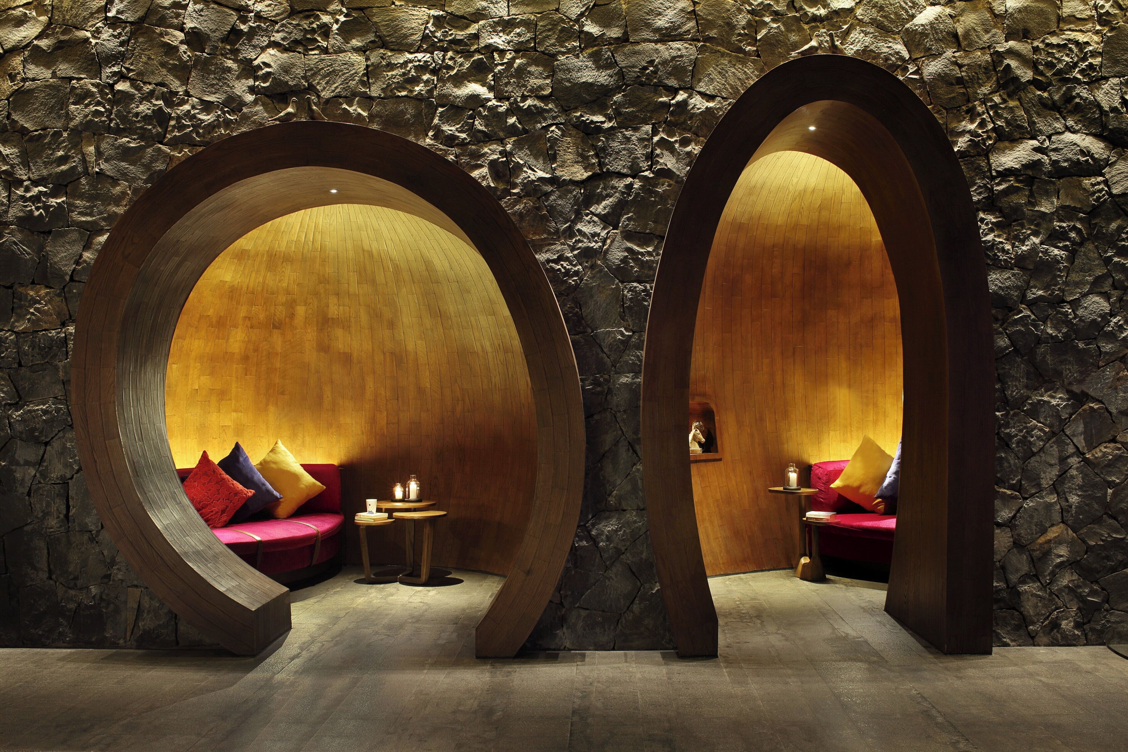 A spa room with two wooden archways, a red sofa, and a small table with candles.