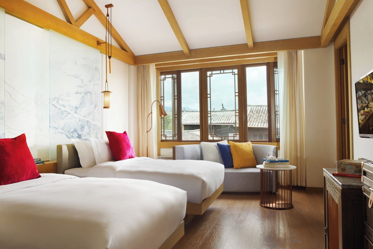 A hotel room with two beds, a small seating area, and a television.