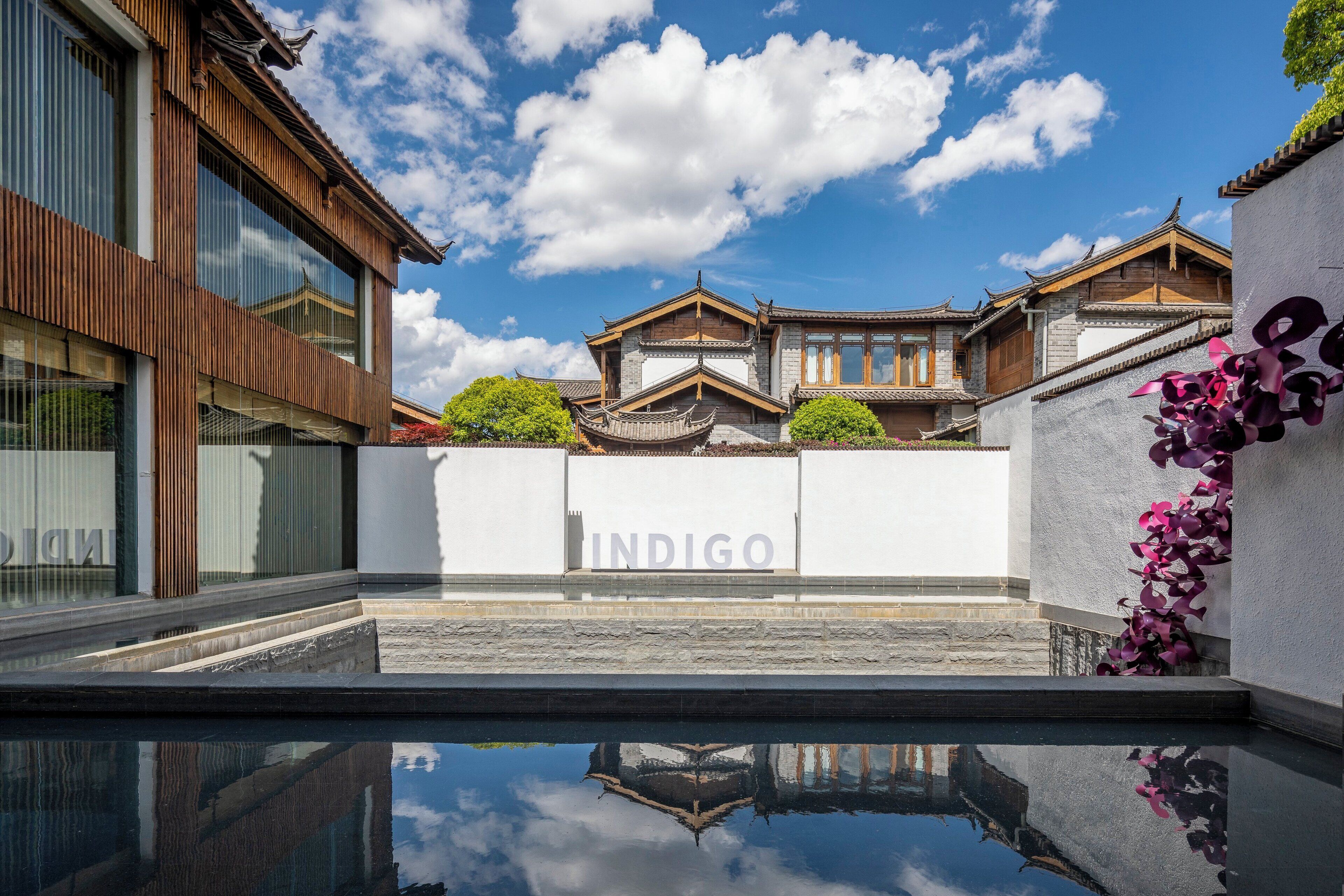 Un bâtiment moderne au style architectural traditionnel, un ciel dégagé et une piscine au premier plan.