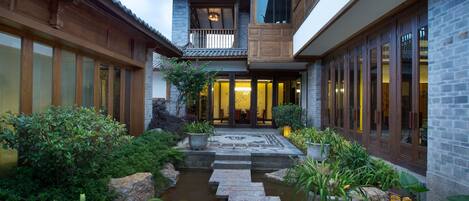A traditional courtyard with a stone bridge, potted plants, and a water feature.