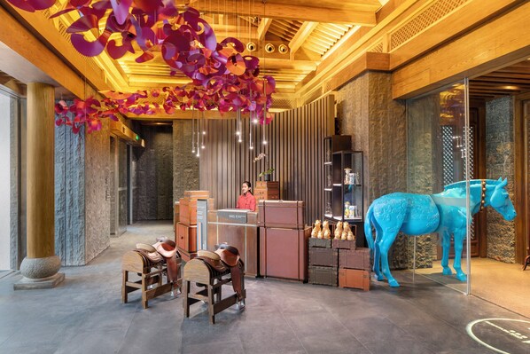A lobby with a wooden ceiling, a receptionist desk, a blue horse sculpture, and vintage luggage.