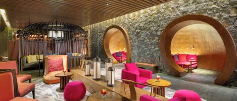 A modern lounge area with wooden ceiling, stone walls, and vibrant pink seating.