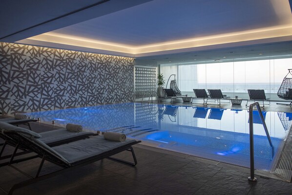 A modern indoor pool with lounge chairs and a patterned wall.