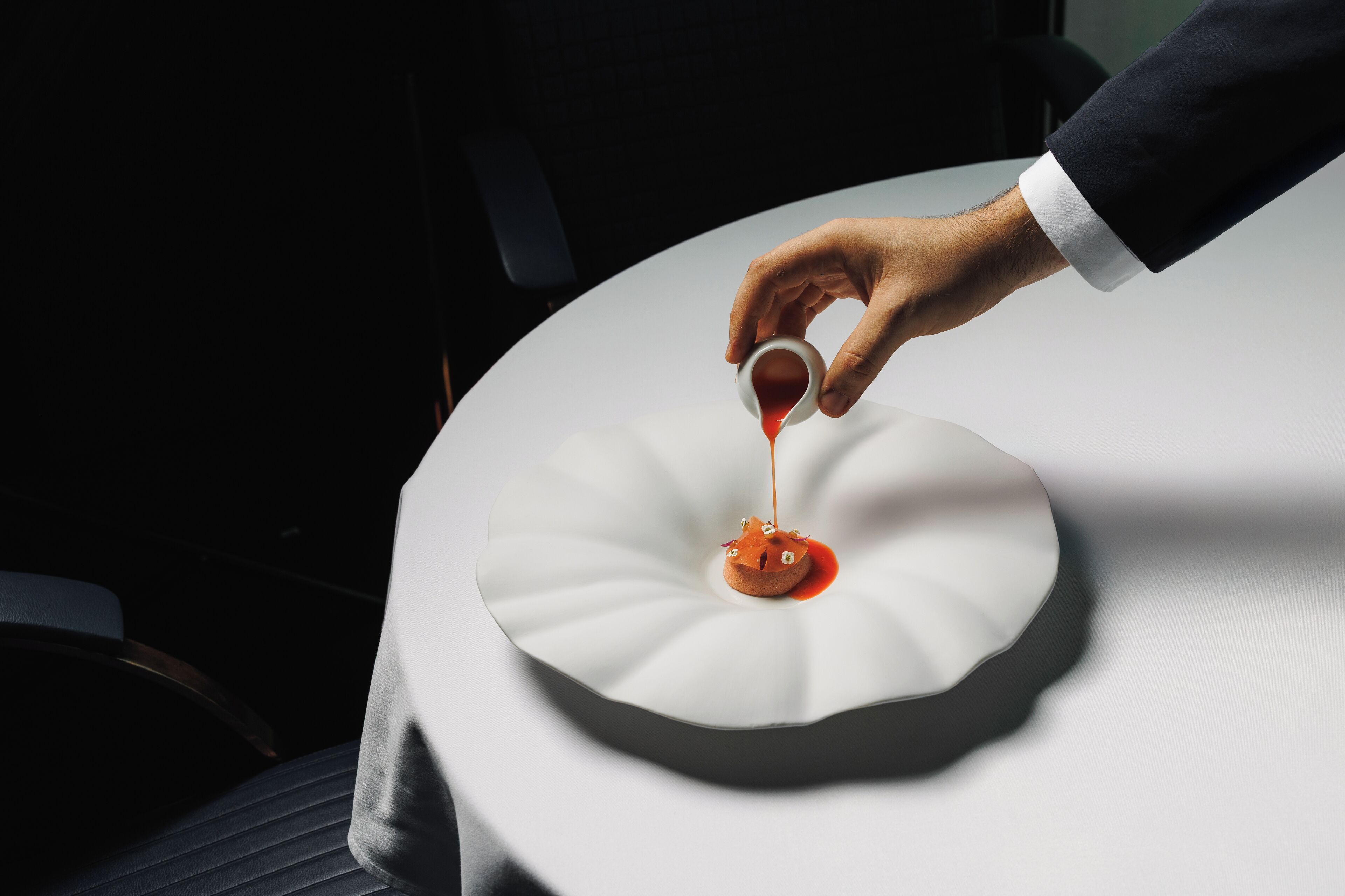 A hand pouring sauce onto a white plate with a unique design.