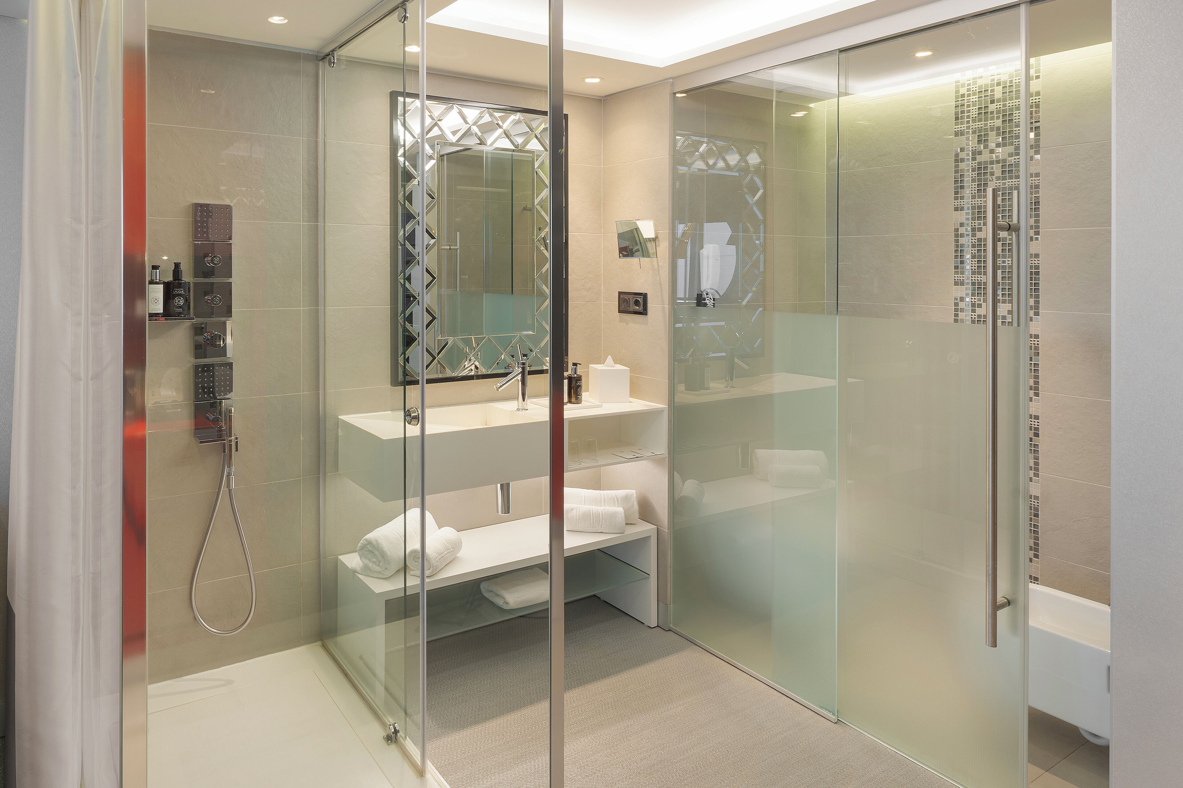 A modern bathroom with a glass-enclosed shower, a glass partition, and a white vanity with a mirror.
