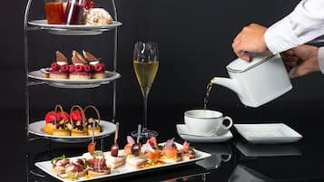 A three-tiered dessert stand with various pastries and a glass of champagne. A hand is pouring a drink into a cup.