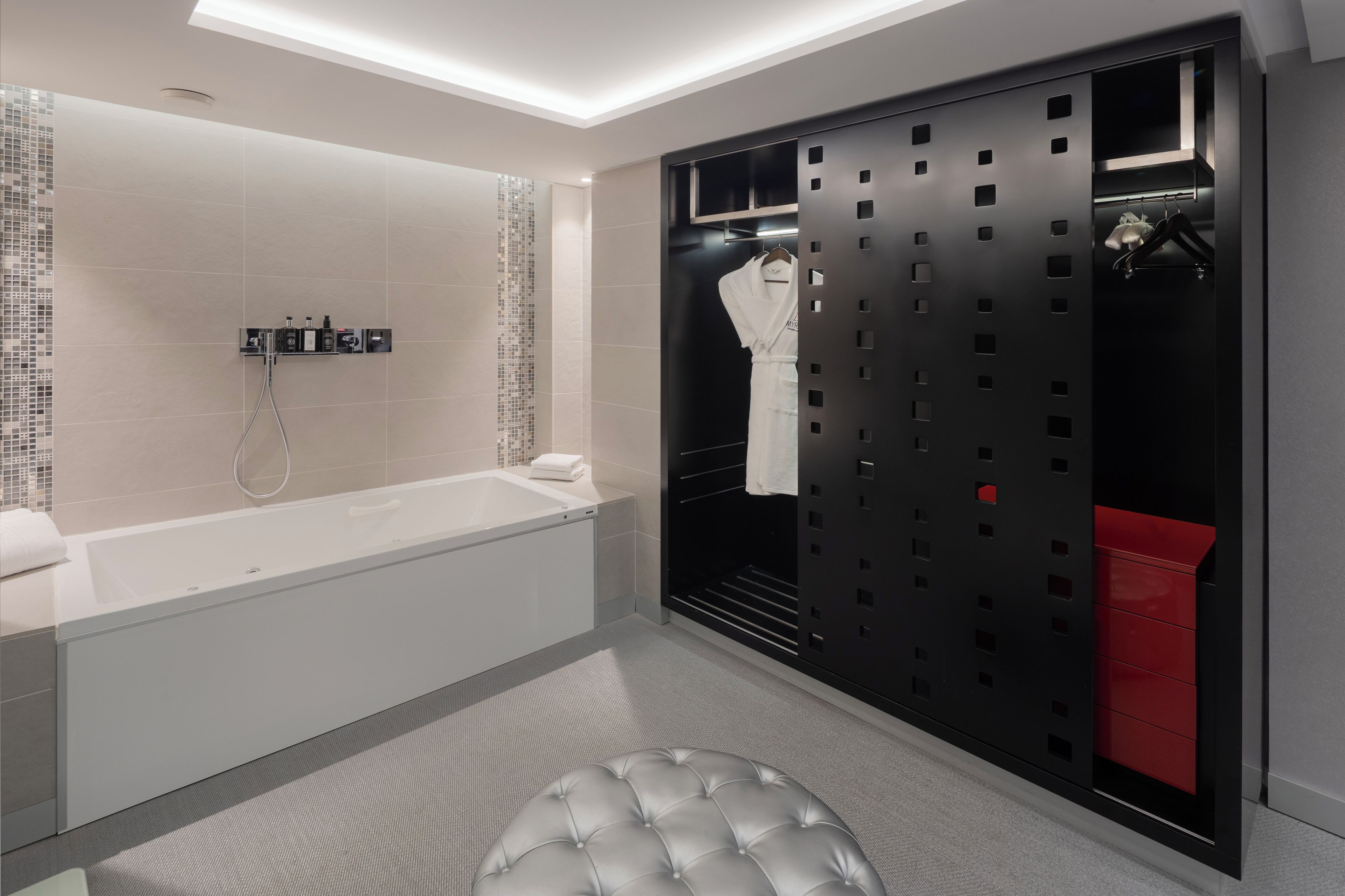 A modern bathroom with a white bathtub, a glass shower enclosure, and a black storage unit with a red drawer.