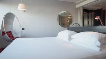 A modern hotel room with a large bed, a hanging chair, a round mirror, and a red desk lamp.