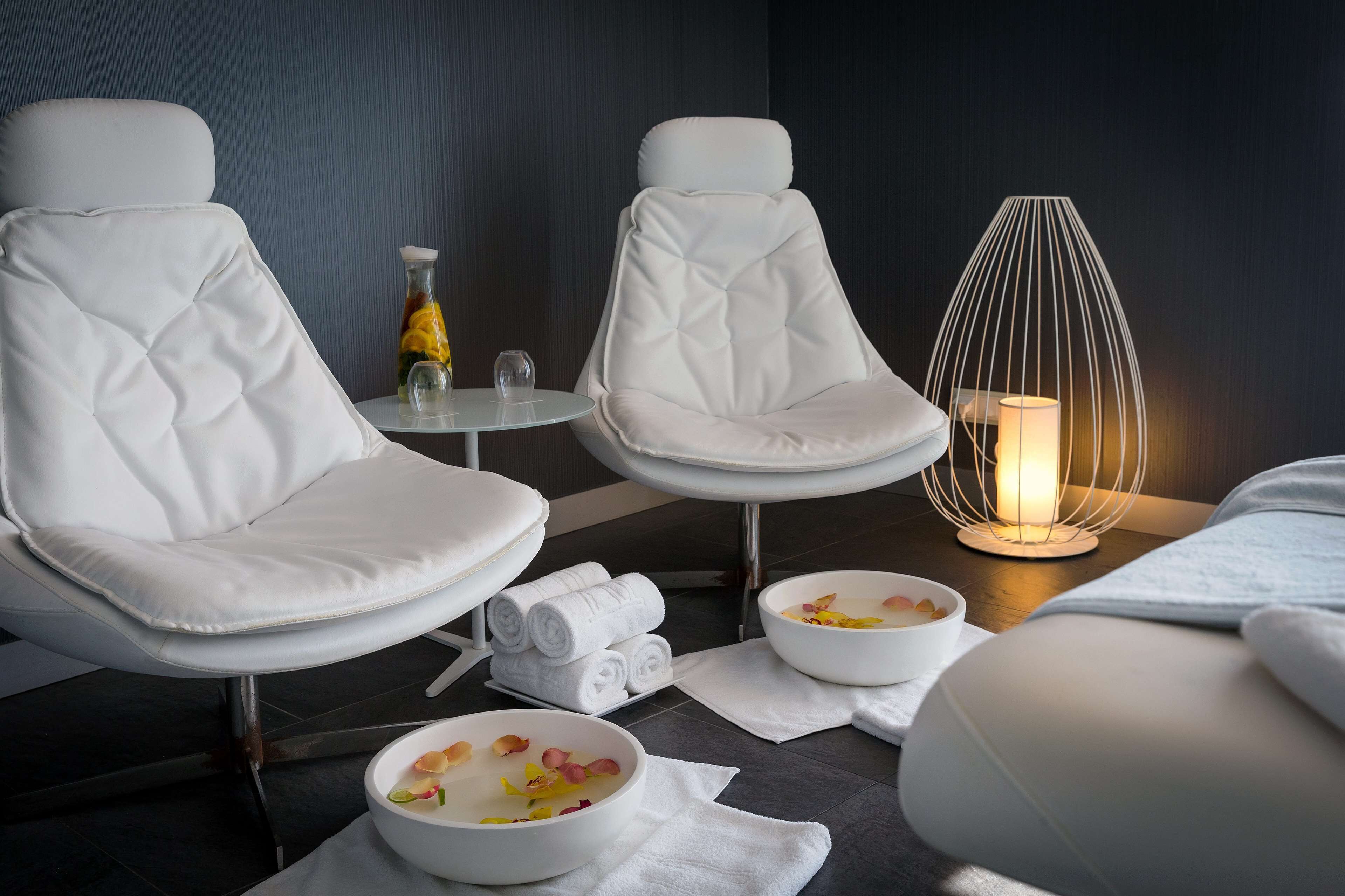 Une salle de bain moderne avec deux fauteuils en cuir blanc, une petite table ronde avec une bouteille et des verres, un porte-serviettes blanc et un bol de sels de bain.