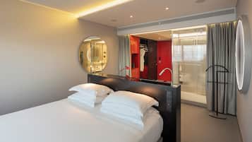 Une chambre d’hôtel moderne dotée d’un grand lit, d’un miroir, d’un dressing et d’un espace douche.