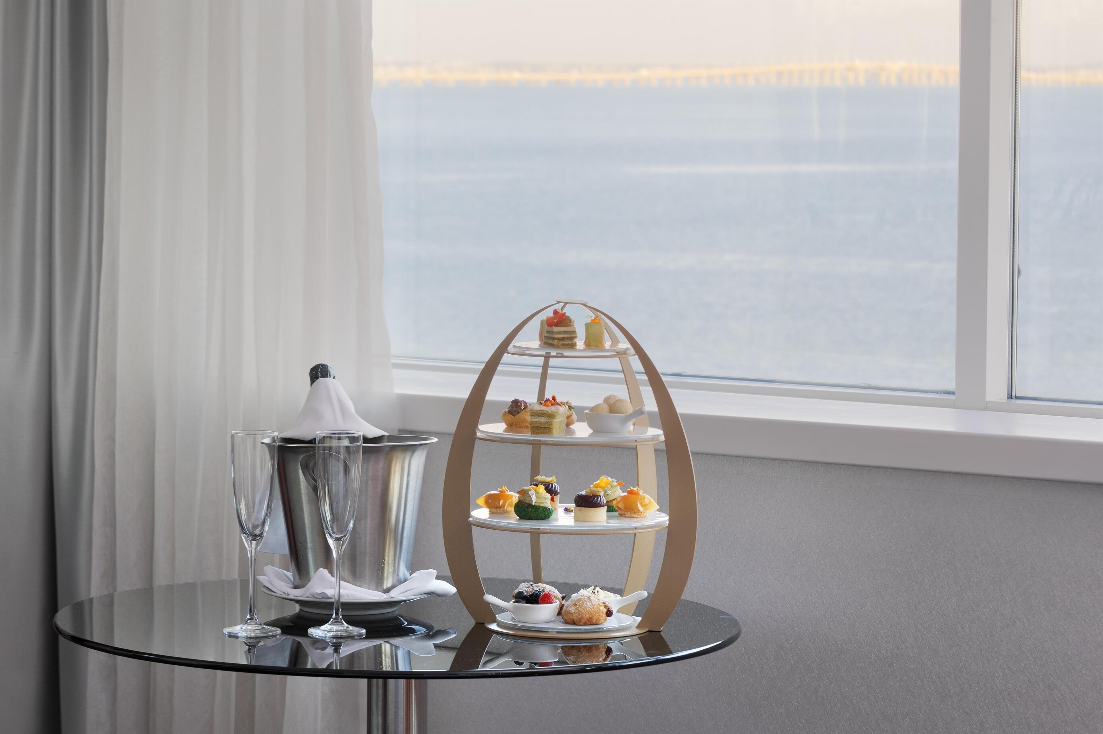 A three-tiered dessert stand with various pastries and a small table with two glasses and a candle.