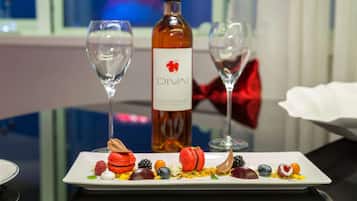 A dessert plate with macarons and berries, a bottle of Divali wine, and two empty wine glasses on a table.
