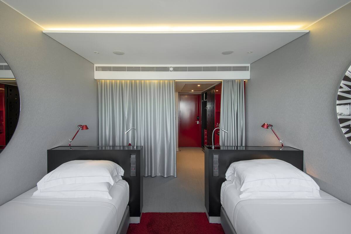 A hotel room with two beds, a red carpet, and a modern design.