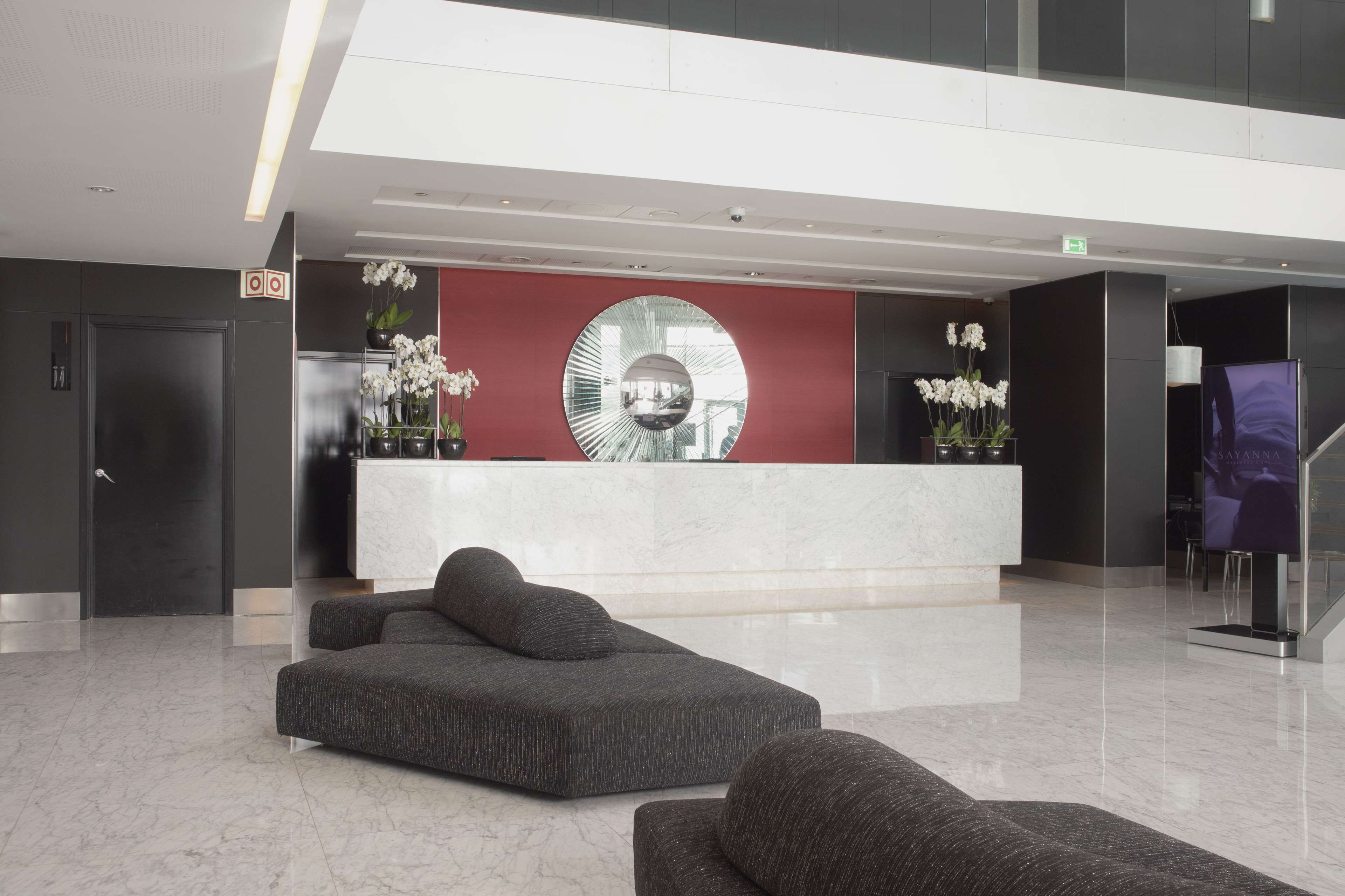 A modern lobby with a reception desk, seating area, and a large mirror.