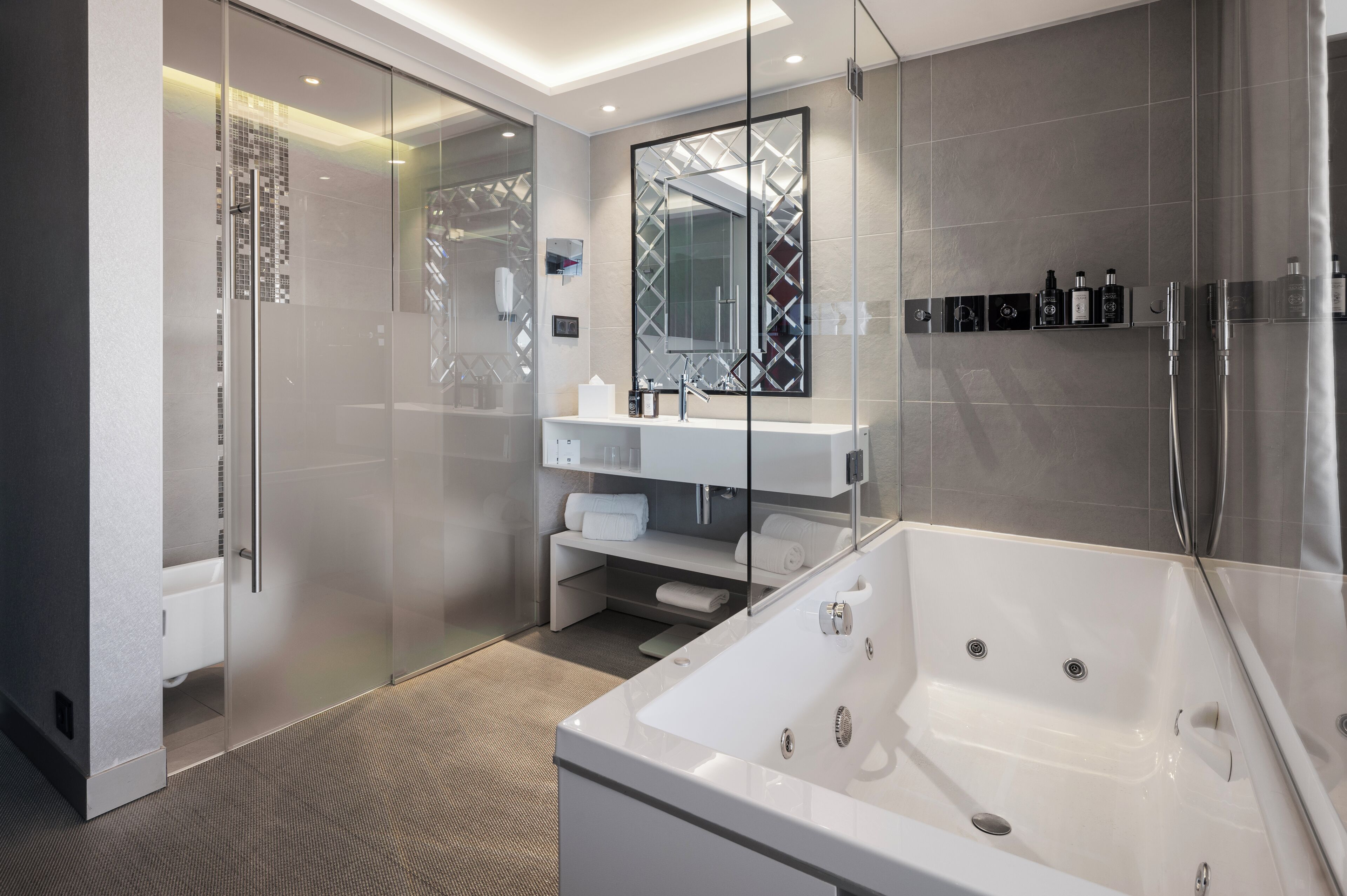 A modern bathroom with a glass shower enclosure, a large bathtub, and a vanity with a mirror.