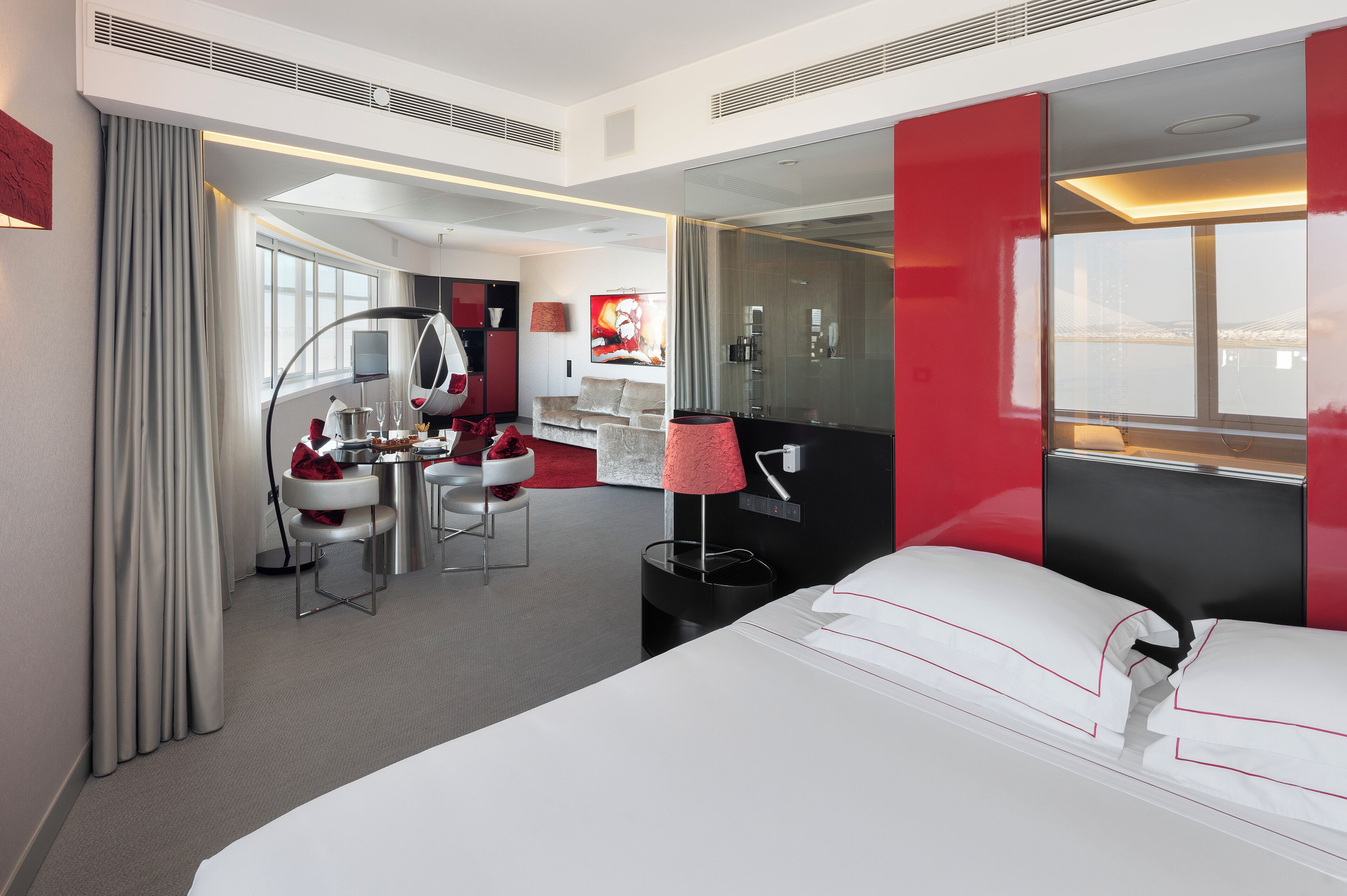 Quarto de hotel moderno com cama, escrivaninha, cadeira, espelho e vista para o exterior.