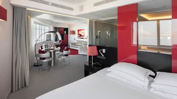 Quarto de hotel moderno com cama, escrivaninha, cadeira, espelho e vista para o exterior.