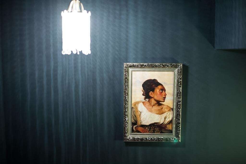 A framed portrait on a dark wall with a white light fixture above it.
