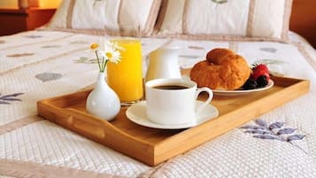 A breakfast tray with a croissant, a cup of coffee, a glass of orange juice, and a small vase with flowers on a bed.