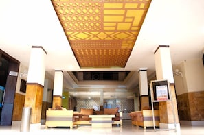 Vestíbulo de hotel con techo estampado, una recepción y una zona de estar.