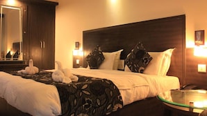Een hotelkamer met een groot bed, een glazen salontafel, een spiegel en een nachtkastje met een lamp.