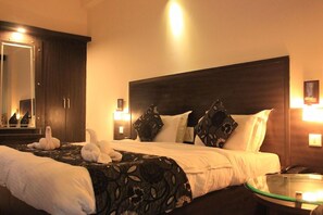 Una habitación de hotel con una cama grande, una mesa de centro de vidrio, un espejo y una mesita de noche con una lámpara.