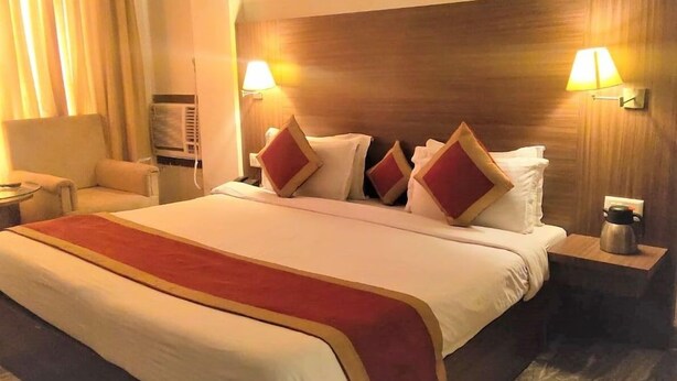 Een hotelkamer met een groot bed, twee bedlampen, een stoel, een klein tafeltje en een heater aan de muur.