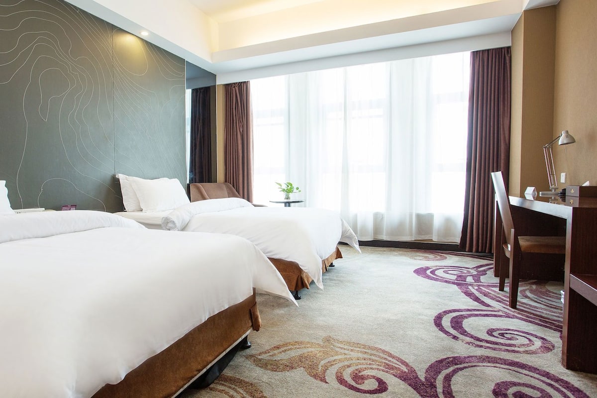 Ein Hotelzimmer mit zwei Betten, einem Schreibtisch, einem Stuhl und Blick auf die Stadt.