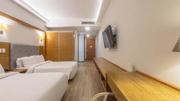 Habitación de hotel con dos camas, un escritorio de madera, un televisor montado en la pared y un armario de madera.