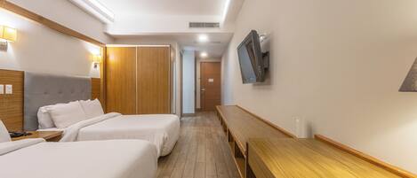 Habitación de hotel con dos camas, un escritorio de madera, un televisor montado en la pared y un armario de madera.